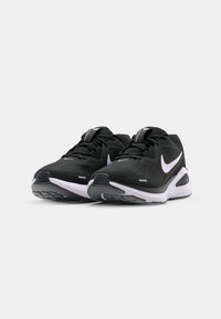 Czarne buty sportowe z teksturowaną cholewką, białymi akcentami, okrągłym czubkiem i grubą podeszwą. Posiadają wyraźne logo Nike oraz sznurowadła.