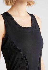 Svart träningslinne med rund halsringning, med mjukt tyg och texturerade meshpaneler på sidan.