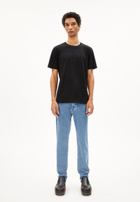 Schwarzes Baumwoll-T-Shirt mit Rundhalsausschnitt, kombiniert mit hellblauen Jeans in geradem Schnitt und schwarzen Clogs. Schlichtes Design und lässige Passform.