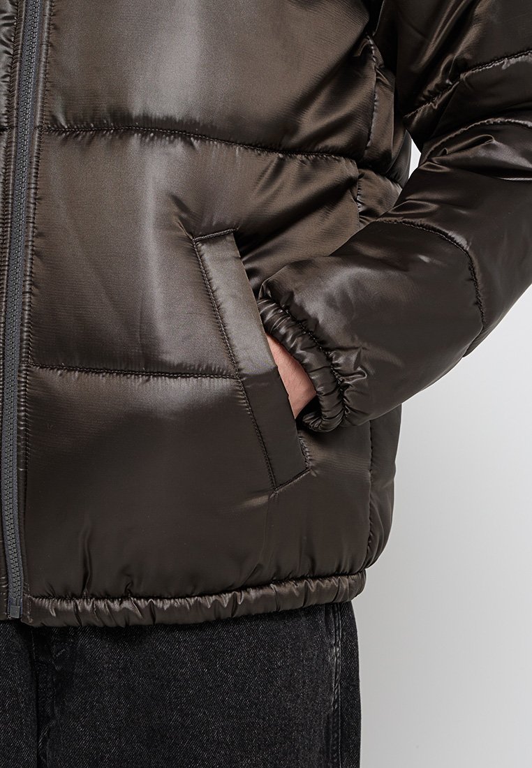 Giacca a vento di piuma lucida marrone scuro con chiusura a zip, dotata di tasca laterale, polsini elastici e orlo a coste per una vestibilità aderente.