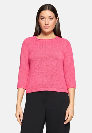 Pull tricoté rose avec un col rond, des manches trois-quarts, une finition texturée et une coupe ample, associé à un pantalon noir.