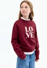 Bordeauxroter Sweatshirt mit dem Wort "LOVE" in hellrosa, Rundhalsausschnitt, langen Ärmeln und gerippten Bündchen. Tragen über einem weißen Hemd mit Kragen.