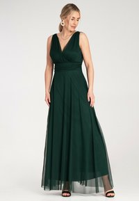Długa zielona sukienka z dopasowanym gorsetem, głębokim dekoltem w kształcie litery V i zwiewnym tiulowym dołem. Posiada szeroki pas w talii i warstwową teksturę.