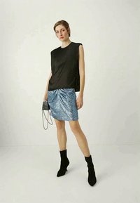 Black sleeveless top paired with a shiny blue sequin mini skirt, black sock boots, and a small handbag with a chain strap.