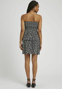 Robe fleurie noire et blanche sans bretelles, avec un ruché au niveau du corsage, une jupe ajustée et une longueur au-dessus du genou. Associée à des sandales à talons noires.