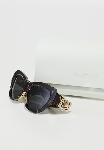 Occhiali da sole Burberry con montatura oversize nera e tartaruga, lenti scure e aste accentuate in oro con un design floreale.
