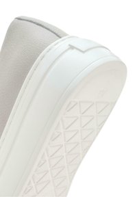 Gros plan sur la semelle d'une sneaker blanche avec un motif géométrique en triangles et une tige en cuir texturé.