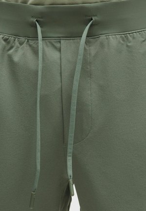 Pantaloni athleisure verzi cu talie elastică, închidere cu șnur și buzunare laterale. Textură moale cu luciu subtil și finisaj neted.