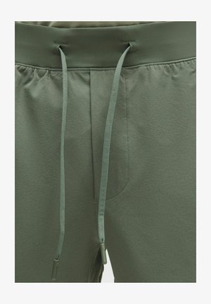 Pantaloni athleisure verzi cu talie elastică, închidere cu șnur și buzunare laterale. Textură moale cu luciu subtil și finisaj neted.