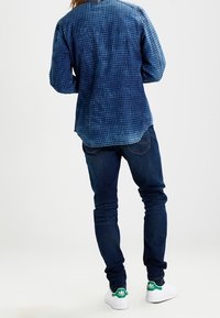 Blå rutiga skjortor, mörkblå jeans, vita sneakers med gröna accenter. Fokusera på tygmönster och färgkontrast.