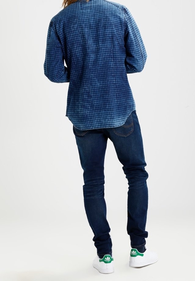 Blå rutiga skjortor, mörkblå jeans, vita sneakers med gröna accenter. Fokusera på tygmönster och färgkontrast.