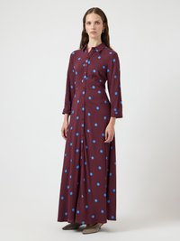 Langes weinrotes Kleid mit blauen Polka-Dots, durchgehender Knopfleiste, Kragen und langen Ärmeln. Glatter Stoff und knöchellanges Design.