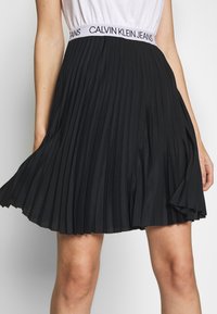 Svart plisserad kjol med en elastisk midja märkta med Calvin Klein Jeans. Har mjukt tyg och en flödande form, lämplig för olika tillfällen.