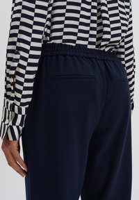 Pantaloni da jogging blu navy con vita elastica e tasche laterali, abbinati a una camicia button-up a righe con righe orizzontali bianche e nere.