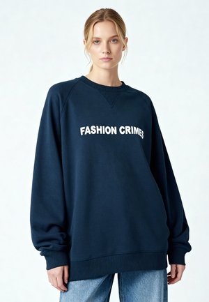 Felpa blu navy con vestibilità oversize, polsini e orlo a coste. Presenta un testo bianco audace "FASHION CRIMES" sul davanti. Tessuto in misto cotone.