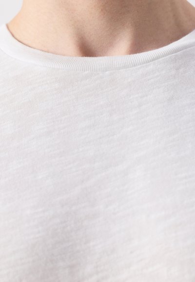 Gros plan sur le cou et le haut de la poitrine d'une personne portant un t-shirt blanc texturé à col rond.