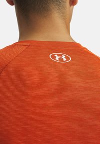 Camisa deportiva roja con un patrón texturizado, con un cuello redondo y un logo blanco en la parte posterior cerca del cuello.