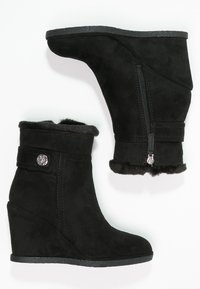 Bottines noires à talon en wedge en daim avec une doublure molletonnée, comportant une fermeture éclair sur le côté et un bouton décoratif sur la sangle de la cheville.