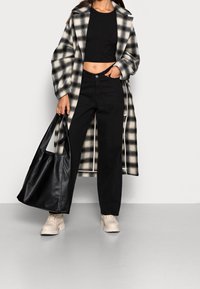 Černobílý kostkovaný dlouhý kabát, černý crop top, černé kalhoty, béžové robustní boty a černá kožená taška.