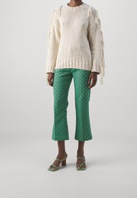 Krämbärgad stickad tröja med fransdetaljer, matchad med gröna mönstrade cropped byxor och gröna klacksandaler. Texturerade och geometriska mönster.