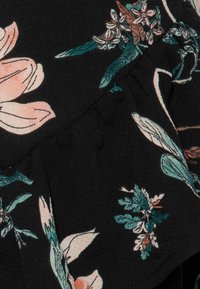 Tessuto nero con superficie texturizzata e stampa floreale nei toni pastello di rosa, verde e beige, con cuciture visibili e pieghe sovrapposte.