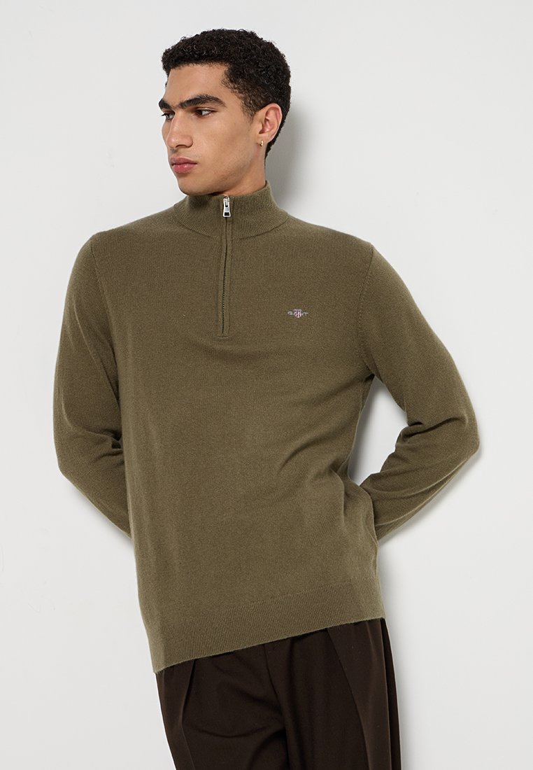 Zielona oliwkowa bluza zapinana na zamek, wykonana z miękkiego materiału, z wysokim kołnierzem i ściągaczami przy mankietach. Mały detal logo na piersi.