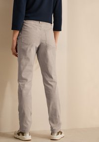 Jeans ajustados de color gris claro con una textura suave, bolsillos traseros y un diseño de pierna estrecha, combinados con zapatillas blancas con acentos oliva.