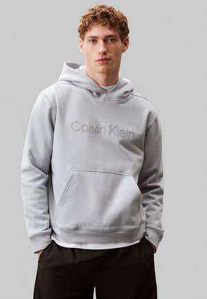 Felpa con cappuccio in cotone grigio chiaro con tasca frontale, cappuccio regolabile con coulisse e logo "Calvin Klein" in rilievo sul petto. Polsini a coste.