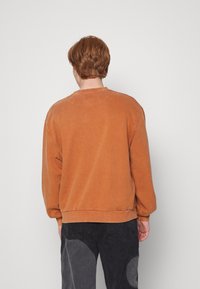 Sudadera de color naranja claro con cuello redondo acanalado y mangas largas. Presenta un corte ligeramente holgado y una tela texturizada.