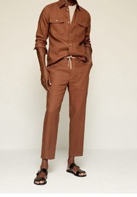 Chemise en lin marron avec deux poches poitrine, assortie à un pantalon ajusté et des sandales noires. Texture douce et design minimaliste.