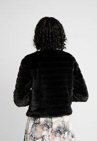 Black faux fur cropped jacket with vertical ribbed texture. Soft finish and rounded collar, worn over patterned snake print pants.