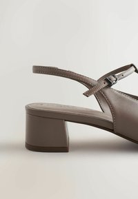 Chaussure à bride arrière en cuir marron avec un talon carré et une bride réglable, présentant une texture lisse et un design minimaliste.
