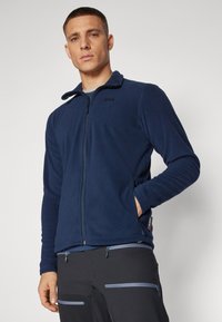 Navy fleece jacket with a stand collar, full zip, side pockets, and logo detail on the chest. Smooth texture, fitted design.
