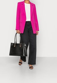 Blazer fucsia entallado sobre una blusa blanca con puntos de lunares, combinado con pantalones negros de pierna ancha y un gran bolso de tote negro con textura de cocodrilo.