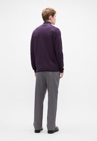 Μωβ μακρυμάνικη μπλούζα με γιακά, συνδυασμένη με γκρι παντελόνι. Η μπλούζα έχει ribbed μανίκια και καθαρό, μινιμαλιστικό σχέδιο. Μαύρα παπούτσια.