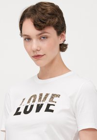 Bílý bavlněný tričko s nápisem "LOVE" v černé barvě a leopardím vzorem. Měkký materiál s klasickým designem kulatého výstřihu.