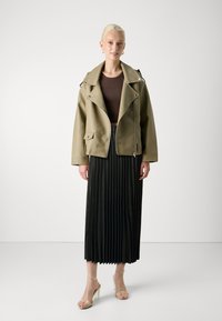 Olive green faux leather biker jacket with silver hardware, paired with a black pleated skirt and clear strap heels. Simple design and textures.
