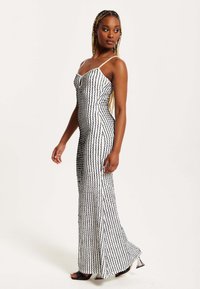 Black and white striped maxi dress with thin straps, fitted silhouette, and textured pattern. Features a subtle side slit and sleek design.