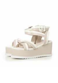 Sandalias de plataforma beige con una amplia suela de goma, que presentan tiras cruzadas y una hebilla en el tobillo fabricada en material sintético.
