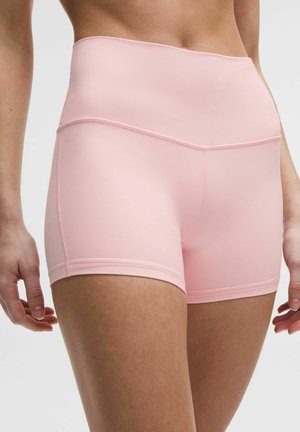 Close-up van een persoon die lichtroze sportshorts met hoge taille draagt, met een glad en aangesloten ontwerp, tegen een neutrale achtergrond.