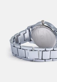 Montre-bracelet en acier inoxydable argenté avec un bracelet à maillons épuré, dotée d'un boîtier rond et d'une couronne proéminente sur le dessus.