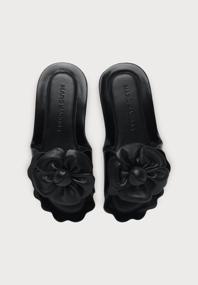 Sandales slides noires avec de grands accents floraux en cuir et des bords festonnés, avec le nom de la marque Marc Jacobs à l'intérieur.