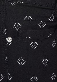 Svart tyg med vita bladmönster, med en liten fickdetalj. Inkluderar en silverfärgad knapp som accent för stängning.