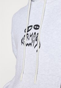 Sweat à capuche gris en mélange de coton, avec une poche avant et des cordons de serrage. Affiche un design graphique noir avec des formes abstraites et du texte.