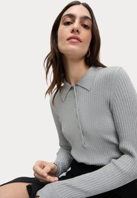 Grijze geribbelde gebreide poloshirt met een kraag, knoopsluiting en lange mouwen, gecombineerd met een zwarte rok; soepele textuur.