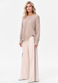 Beżowy, oversize sweter z prążkowanymi mankietami i dołem, połączony z kremowymi spodniami o szerokich nogawkach, z kontrastującymi pionowymi paskami. Teksturowana tkanina.