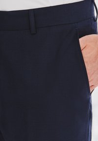 Granatowe spodnie o gładkiej fakturze, z dopasowaną talią i bocznymi kieszeniami. Tkanina wydaje się lekka i strukturalna.