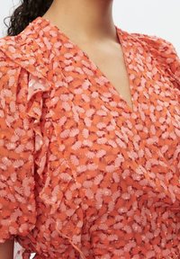 Vestito floreale sfrangiato in arancione e rosa, con scollo a V profondo e tessuto strutturato con piccoli motivi in rilievo ovunque.