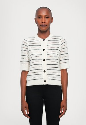Cárdigan blanco de punto con mangas cortas, presenta rayas horizontales negras y detalles de calado, abrochado con botones negros.