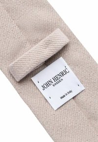 Beige geweven stof met een textured patroon, voorzien van een wit label met de tekst "John Henric Sweden, Made in Italy."